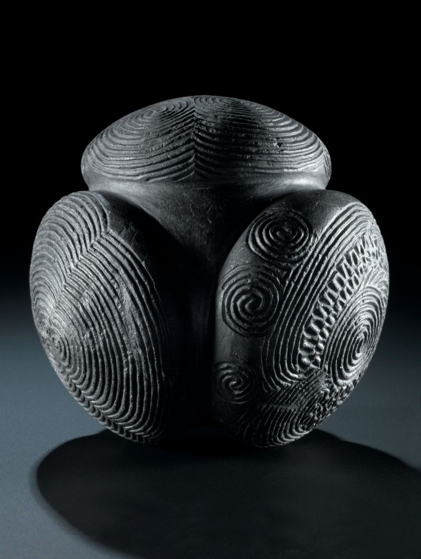 Dark stone ball with four rounded knobs covered in carved spirals and concentric rings