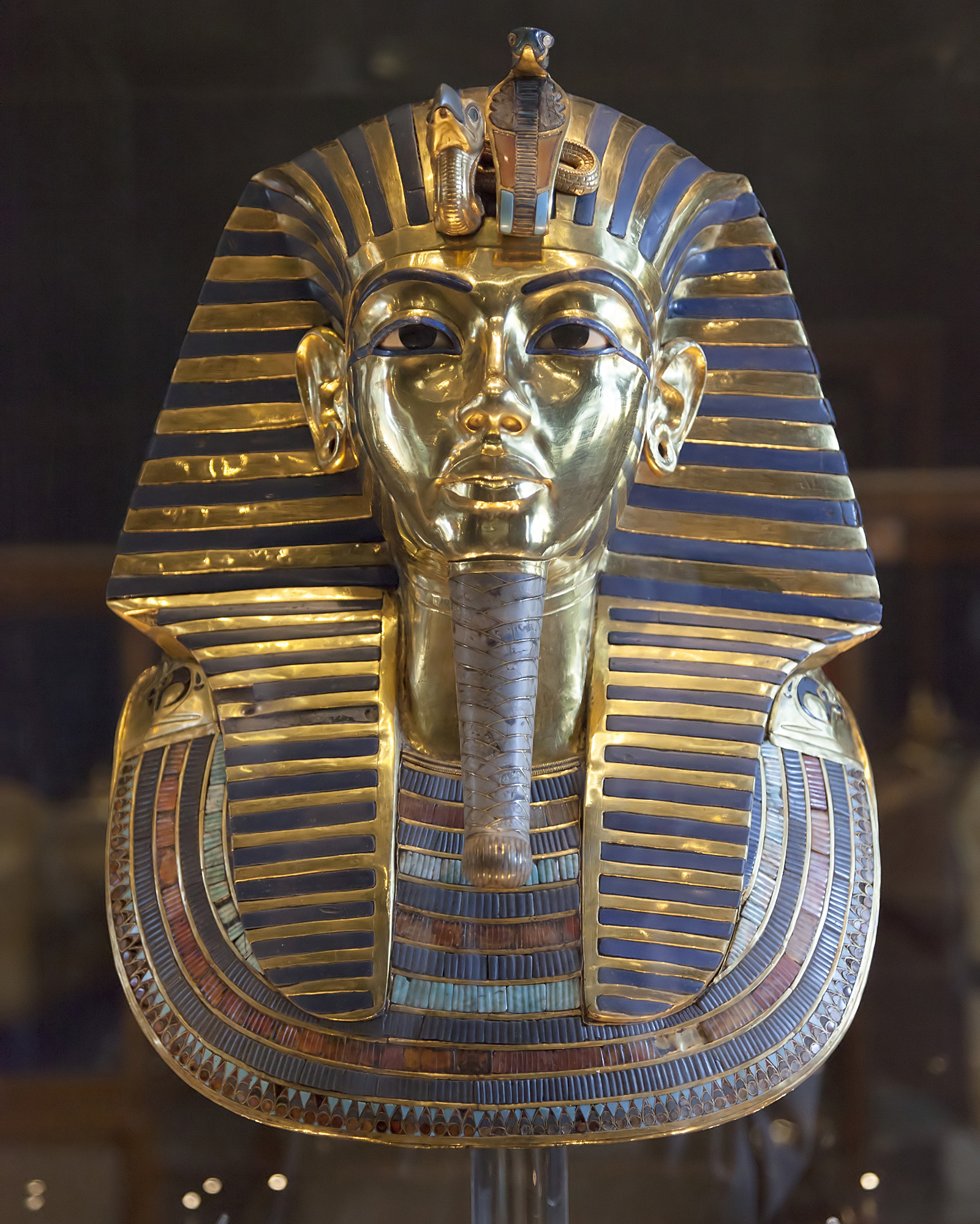 Gold funerary mask with a blue-striped headdress, a cobra and vulture on the brow and a long plaited beard